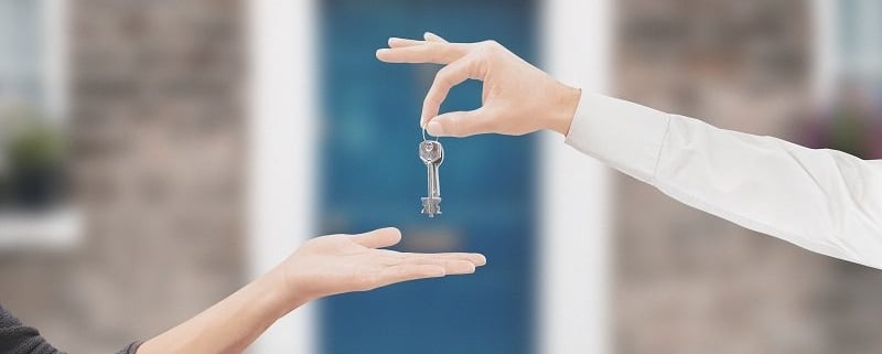Two people exchanging keys in front of house.
