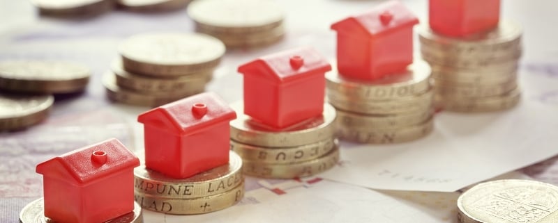 Miniature houses resting on pound coin stacks concept for property ladder, mortgage and real estate investment.