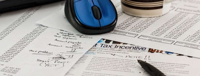 A stack of tax papers with a pen and computer mouse resting on top.