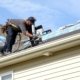 Male construction worker on the roof of a house repairing shingles with a nail gun on a house falling apart.